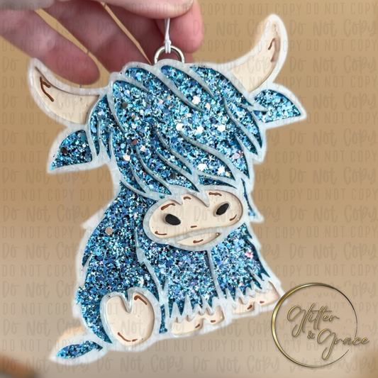 vehicle air freshener shaped like a highland cow decorated with blue glitter and tan accents