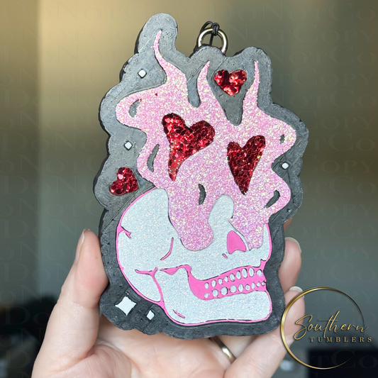 vehicle air freshener with the image of a skull with flames coming from eyes and hearts decorated with pink white and red glitter for a valentine theme