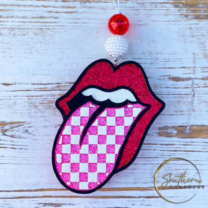 vehicle air freshener decorated with red what and pink glistening glitter in the shape of lips sticking out tongue with checker print on tongue  