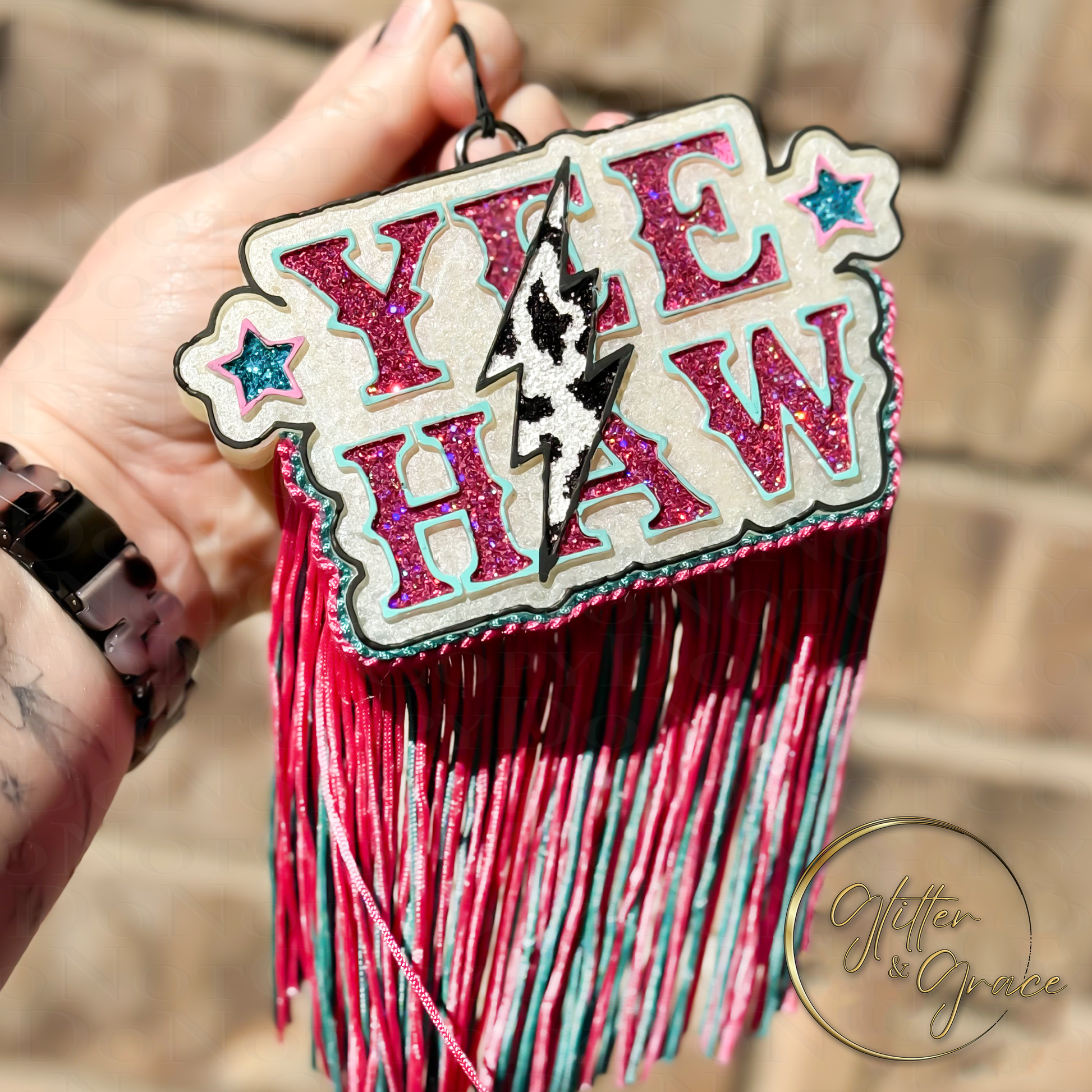 vehicle air freshener saying yee haw with pink and teal glitter with a lightning bolt in the center with cow print and fringe